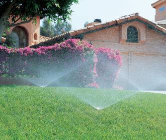 Lawn sprinklers in action in front of a house.